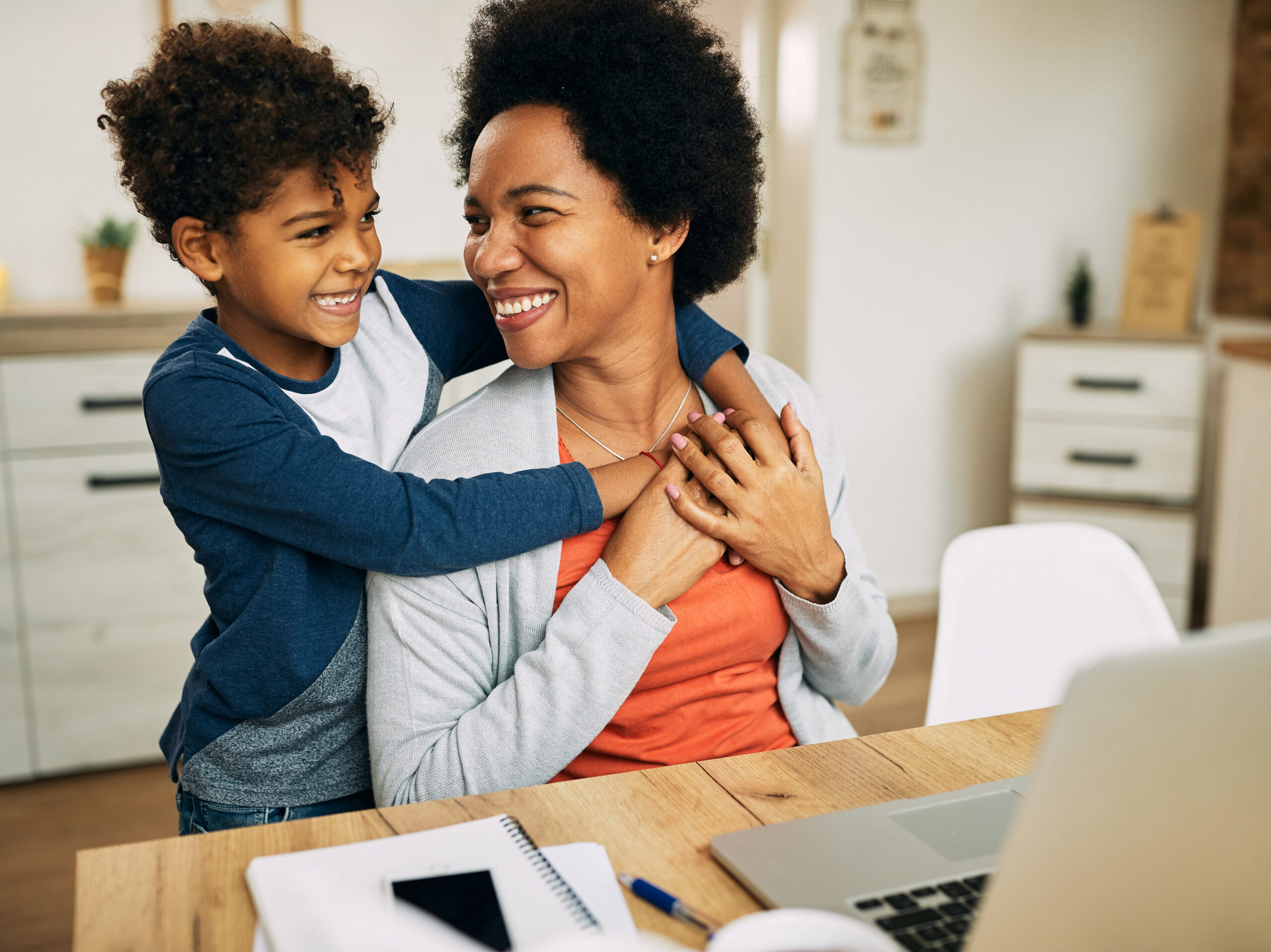 Mother embracing her son while working on a computer.