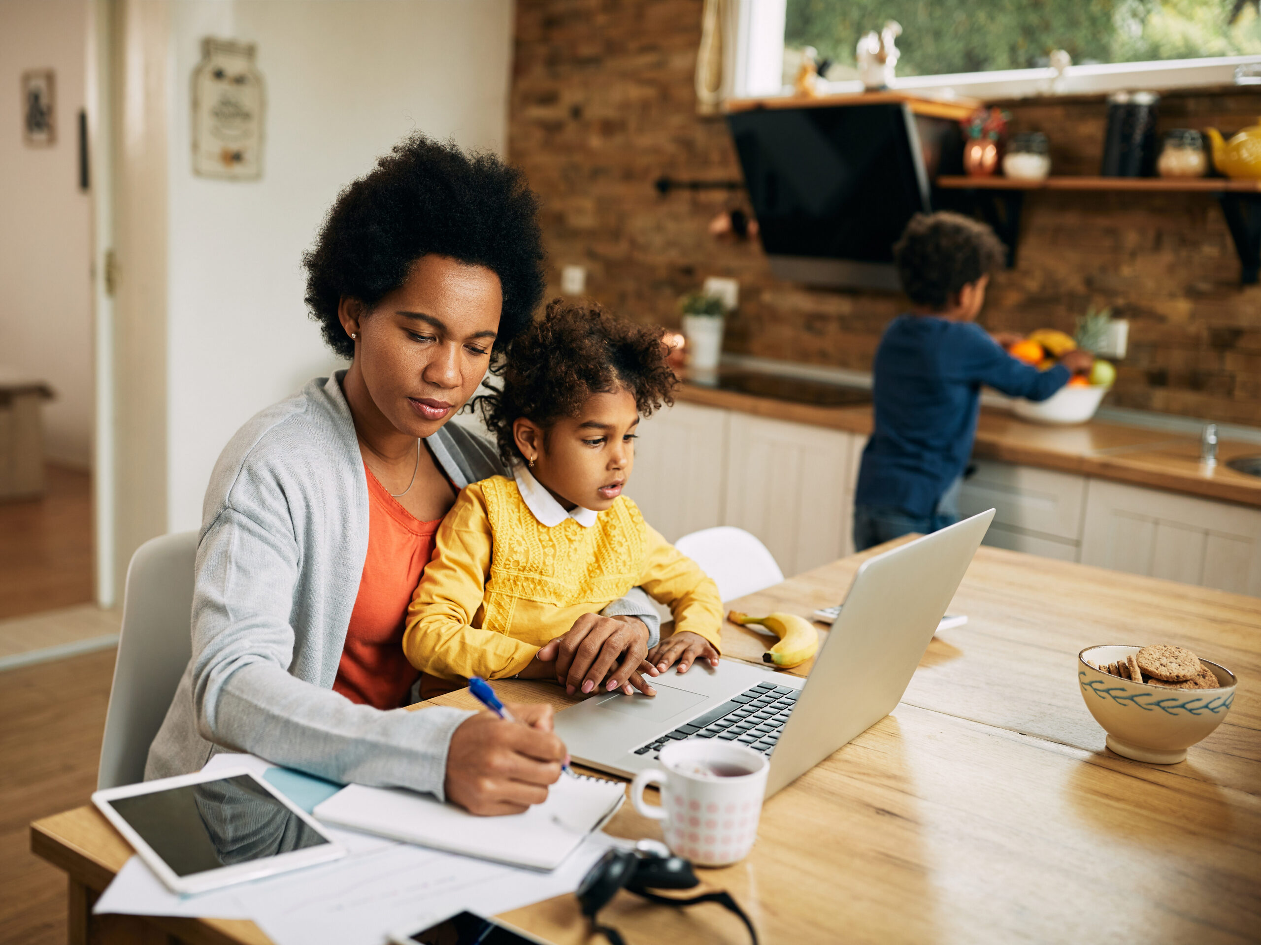 Working mother taking notes while her daughter is sitting on her lap.